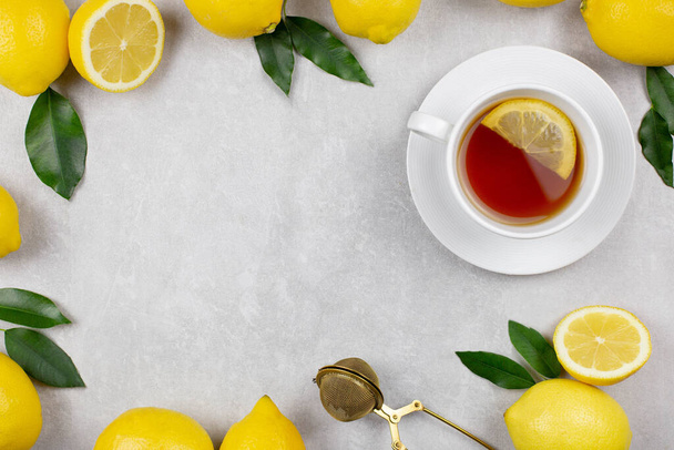 Cup of tea with fresh lemons and leaves on white concrete stone background. Hot healthy beverage. Immune defence, vitamin c. Top view. Copy space. - Photo, image