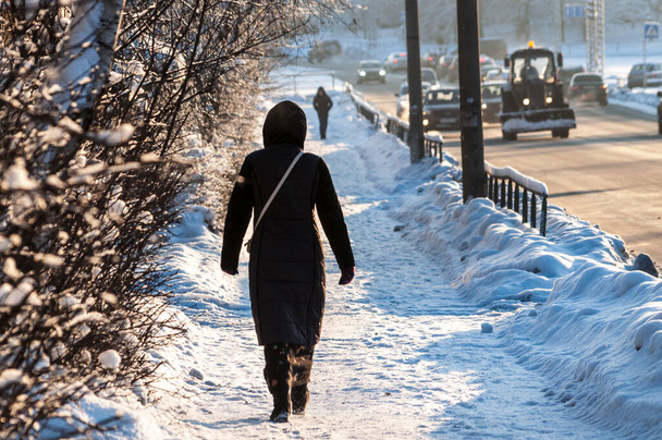 女性は雪に覆われた都市道路を歩いている。バックビュー。高品質の写真 - 写真・画像