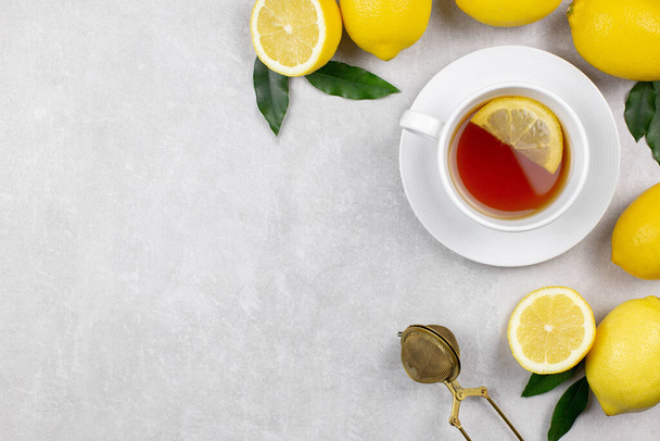 Kopje thee met verse citroenen en bladeren op witte betonnen achtergrond. Warme gezonde drank. Immuunverdediging, vitamine C. Bovenaanzicht. Kopieerruimte. - Foto, afbeelding