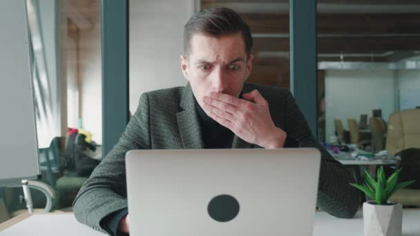 Zszokowany biznesmen otrzymał złe wieści na laptopie podczas pracy w biurze. Przerażony człowiek czyta złą wiadomość, zakrywa usta strachem. Koncepcja kryzysu i upadłości. - Materiał filmowy, wideo