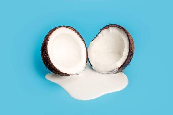 Crema de coco o mantequilla con coco fresco sobre fondo azul. Zumo de crema blanca goteando de coco. - Foto, Imagen