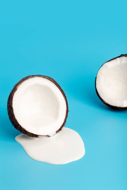 Crema de coco o mantequilla con coco fresco sobre fondo azul. Zumo de crema blanca goteando de coco. - Foto, imagen