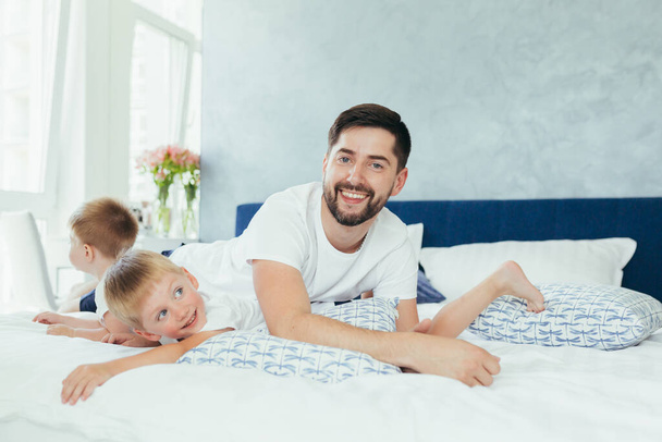 husband father playing with his children, two little boys brothers, in a large bedroom - Foto, imagen