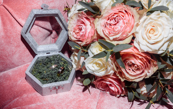 white gold wedding rings in a box and a bridal bouquet of delicate roses and greenery - Foto, Bild
