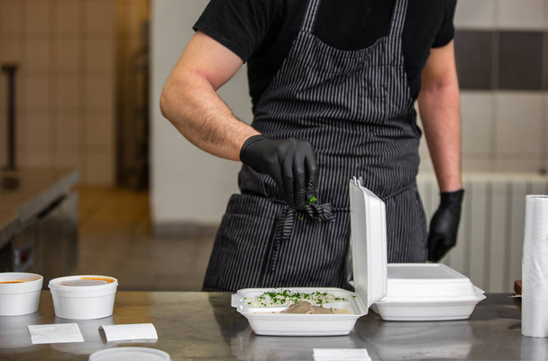 Chef preparing dish to a box in the restaurant for food delivery service to home, online ordering - Foto, afbeelding