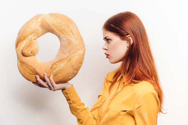 nő kezében egy kerek kenyér a kezében egy könnyű háttér egy sárga ing kivágott kilátás - Fotó, kép