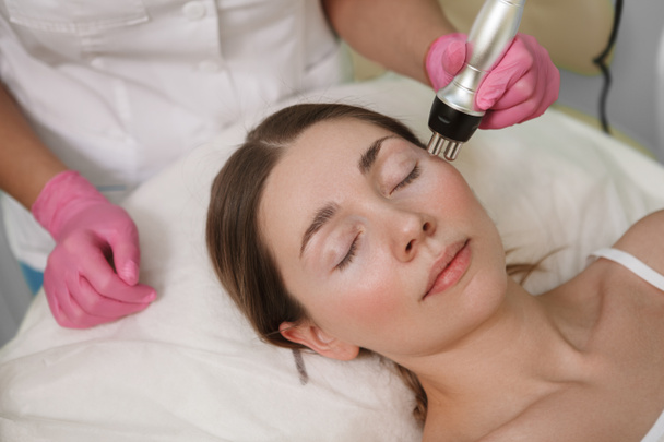 Крупный план женщины, расслабляющейся в салоне красоты, получающей профессиональную процедуру для лица - Фото, изображение
