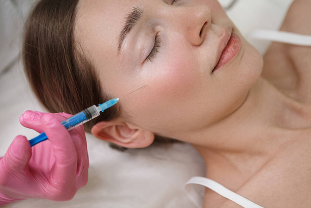 Gebeten close-up van een vrouw krijgen wang vuller injecties in schoonheidskliniek - Foto, afbeelding