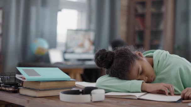 Panning slow-motion medium shot van moe afro meisje viel in slaap aan het bureau in de woonkamer tijdens het doen van huiswerk op school - Video