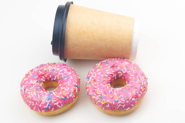 Zwei leckere Donuts mit Einweg-Kaffeetasse auf weißem Hintergrund - Foto, Bild