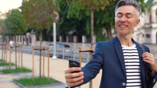 Caucasian handsome middle-aged businessman walking the street and talking on mobile phone with videochat. Man strolling and speaking on cellphone via webcam. Busy male video calling. Videochatting. - Footage, Video