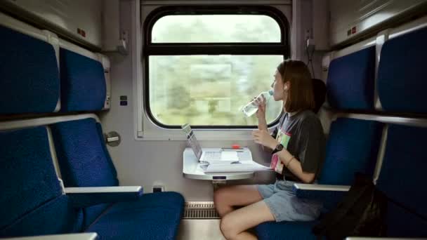 Freelancer feminino trabalhando no laptop e com documentos no compartimento do trem enquanto se move à mesa, usando fones de ouvido sem fio. - Filmagem, Vídeo
