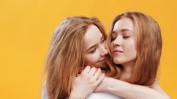 Retrato de cerca de dos hermanas gemelas abrazadas, disfrutando de su conexión, fondo de estudio naranja - Imágenes, Vídeo