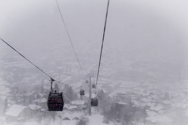 Teleferik sisli bir kar fırtınası sırasında teleferikten fotoğraflandı. Kışın kar yağarken Saraybosna teleferiği. Kış ve kar. Kar yağıyor. - Fotoğraf, Görsel