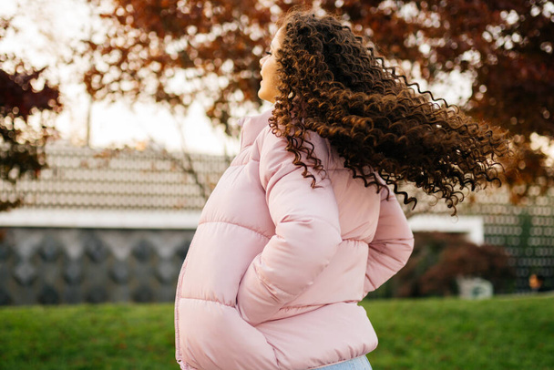 view from the back in a half-back close-up. A girl in a warm pink jacket plays with her hair spreading them behind her back with head turns - Foto, immagini