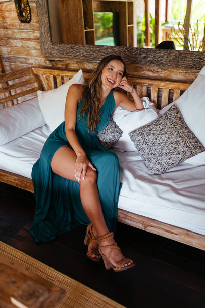 estélyi ruha egy vágott csupasz lábbal egy mosolygó lány ül az ágyon egy bungalóban - Fotó, kép