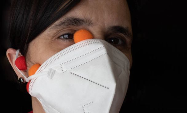 žena s bílou maskou ffp2 chránící před Covid19 s gumičkou v uchu zkříženou a s barevnými viry vycházejícími z důvodu jeho špatné polohy na černém pozadí koronavirového konceptu. - Fotografie, Obrázek