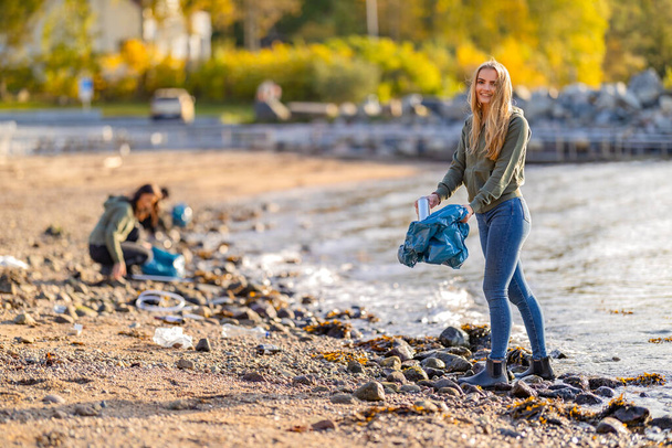 Engagierte, lächelnde junge Freiwillige reinigen an sonnigen Tagen den Strand nach Plastik - Foto, Bild