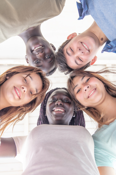 Pohled nahoru na teenagery, jak se spolu usmívají v kruhu. Multietničtí přátelé šťastný, freindship a antiracism koncept. - Fotografie, Obrázek