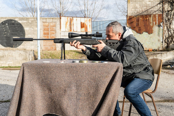 Adult caucasian man shooting Black polymer frame modern Air gun pellets with optics on the table outdoor side view - Photo, Image