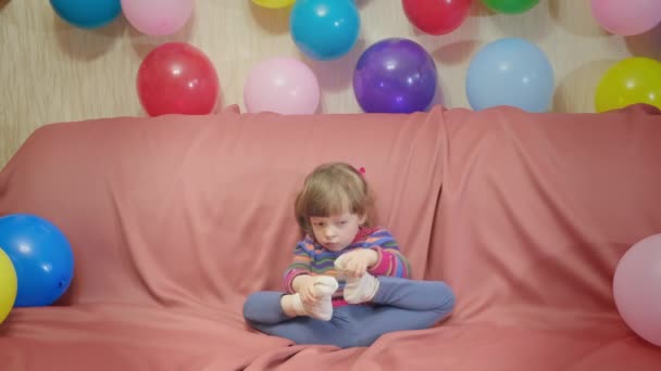 Cute little girl playing with her feet. There are a lot of balloons around - Footage, Video