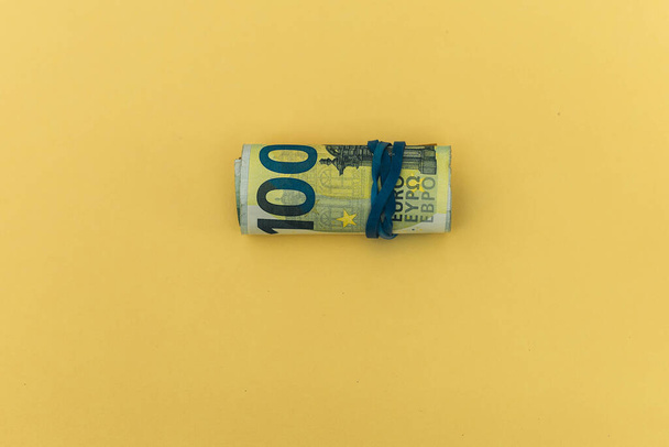 enfoque selectivo de un rollo de ciento y otros grandes billetes en euros sobre un concepto de fondo amarillo de economía, ahorro y crisis económica - Foto, imagen