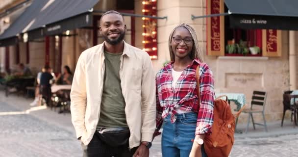 Portré fiatal boldog afro-amerikai pár áll a szabadban a városban kéz a kézben, és nézi a kamerát. Férfi és női touists mosolyog és pózol a kamerába a városban. Dolly lőtt. Közelítés. - Felvétel, videó