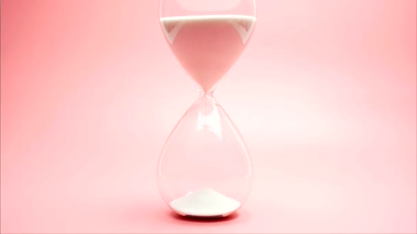 Close up, The hourglass and white sand are in a glass jar. The sand is all flowing down, time is running out. On the pink background. - Felvétel, videó