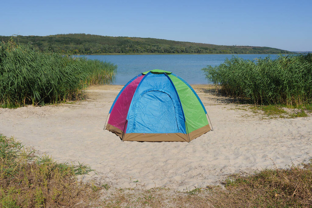 Kukaan lähellä camping teltta sijaitsee hiekkaranta joella paikallisessa vaellus yksinäisyys luonto. Värikäs kupoli teltta järven rannalla tai retkeilyvälineet matkustaa. Retkeilyteltta ekomatkailuun tai kalastukseen - Valokuva, kuva