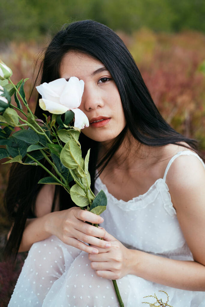 Close up - Portret młodej Azji długie ciemne włosy kobieta panna młoda gospodarstwa biały kwiat róży siedzi na polu. Retro. - Zdjęcie, obraz