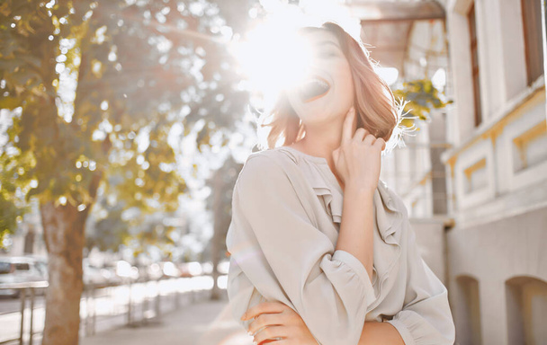 szczęśliwy blondynka dziewczyna z jasny makijaż w pobliżu budynku gestykulując z rąk modny styl ubrania - Zdjęcie, obraz