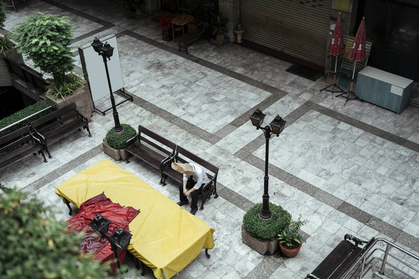 Bolso de papel hombre sentado en un banco en la plaza del jardín de la ciudad. Lonely bolsa de papel hombre sentado solo en la ciudad. - Foto, imagen