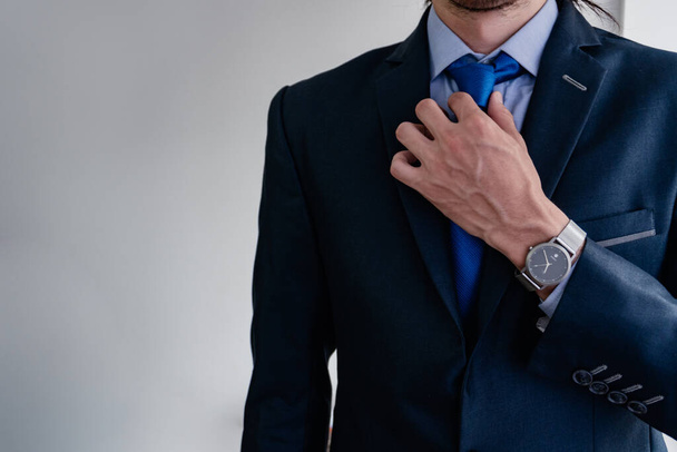 biznesmen dopasowuje swój niebieski krawat do swojego monochromatycznego garnituru swoją żylastą i bardzo męską dłonią, pokazując swój tytanowy zegarek. - Zdjęcie, obraz