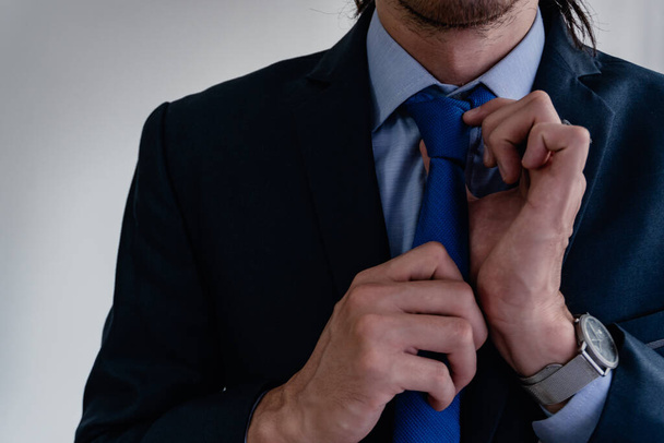 Geschäftsmann, der sich von zu Hause aus auf die Arbeit vorbereitet, seine Krawatte justiert, hellblaues Hemd trägt, blaue Krawatte und blauen Anzug, einfarbig - Foto, Bild