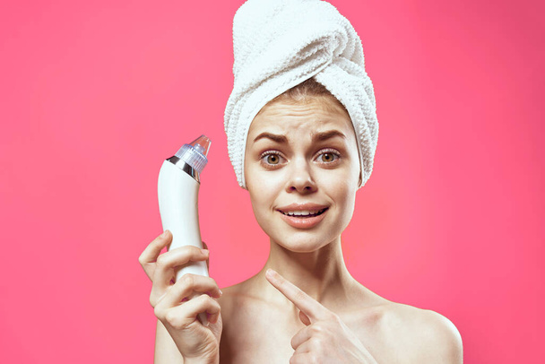 cheerful national woman with a towel on her head massagers in hands skin care spa treatments pink background - Foto, afbeelding