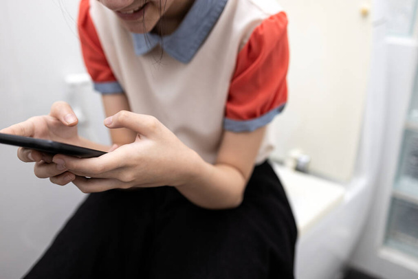 携帯電話で遊ぶゲーム、ソーシャルネットワークや友人とチャットを使用してアジアの学生は、メッセージを送信し、学校でトイレのボウルに座って、怠惰な女の子の研究の生活、学校をスキップし、時間の間にクラスをスキップして学ぶために - 写真・画像