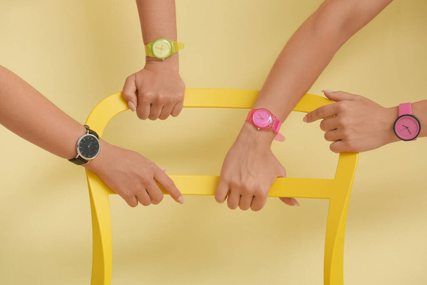 Manos femeninas con relojes de muñeca sosteniendo silla cerca de la pared de color - Foto, imagen