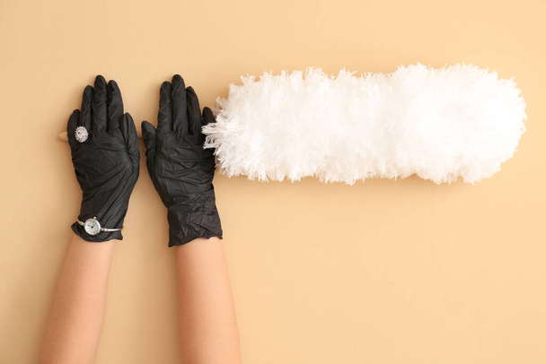 Female hands in rubber gloves, ring and wrist watch with dust brush on color background - Photo, Image