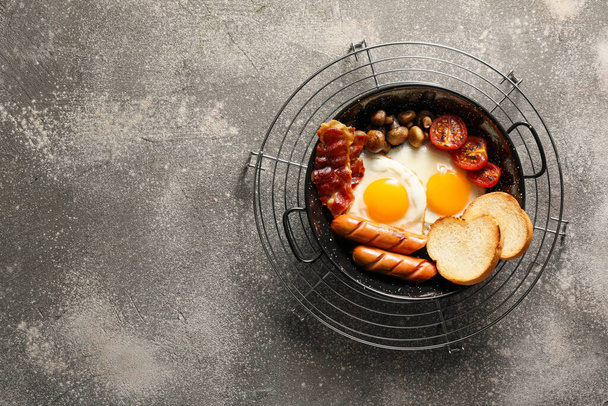 Traditional English breakfast with fried eggs in pan on gray background - Photo, Image