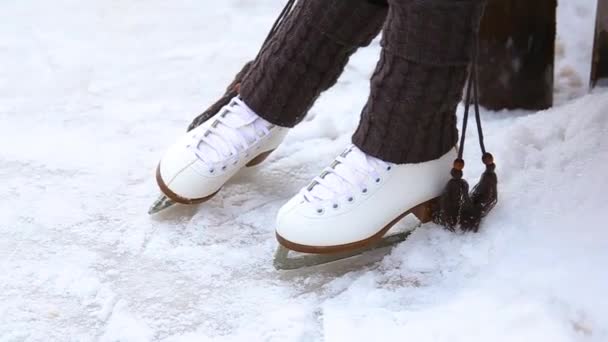 A child in figure skates on the rink sits on a bench and dangles his legs. Legs close up. Ice skating in winter - Footage, Video