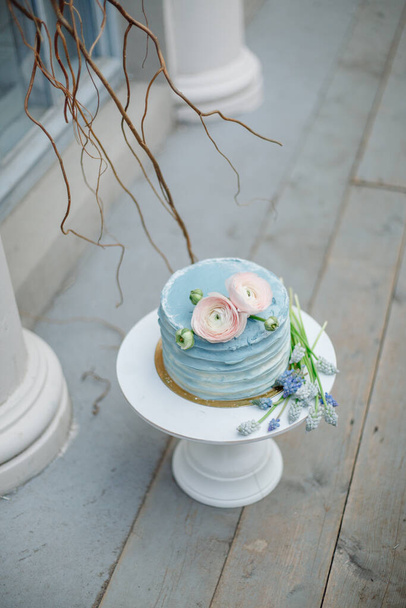 Wedding cake with soft blue cream and decorated with fresh flowers on a white stand. - Фото, изображение