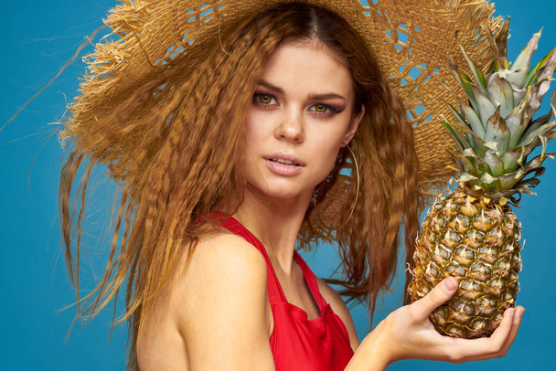 A woman in a straw hat with a pineapple in her hands or is it a fun blue exotic fruits background - Fotó, kép