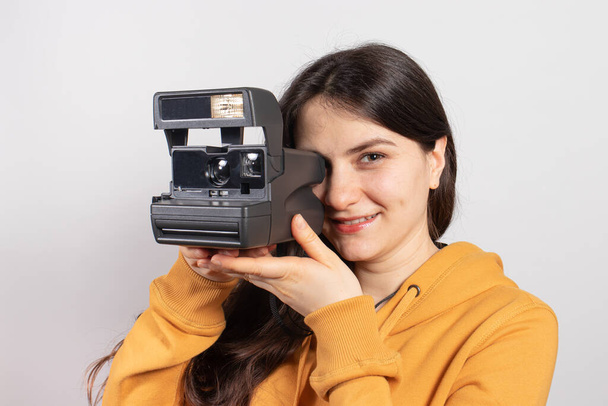 Krásná brunetka drží fotoaparát a fotí, usmívá se na bílém pozadí. Ženský fotograf, kurzy a fotografický trénink. - Fotografie, Obrázek