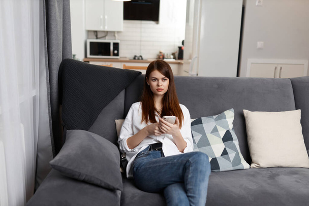 jolie femme avec un téléphone dans ses mains assis à la maison dans un appartement intérieur - Photo, image