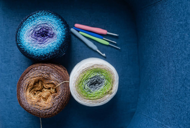 Balls of yarn in different colors and spokes are lying on a blue chair. Top view. Female hobby. - Photo, Image
