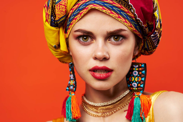 žena na sobě pestrobarevné turban dekorace atraktivní vzhled etnicity červené pozadí - Fotografie, Obrázek