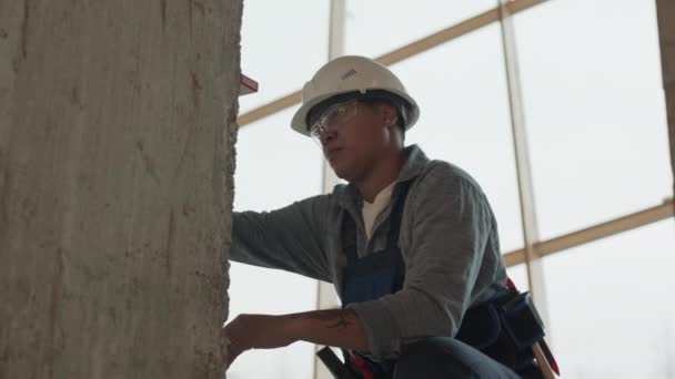 низкоугольная средняя длина смешанной расы женщин-строителей носить защитные очки и шлем, с использованием пузырькового уровня инструмент на бетонных столбов в процессе строительства - Кадры, видео
