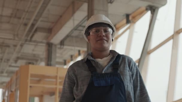 Low angle arc medium point of view of Mixed-Race female builder wearing protective goggles and helmet, standing in house under construction, looking on camera - Materiał filmowy, wideo