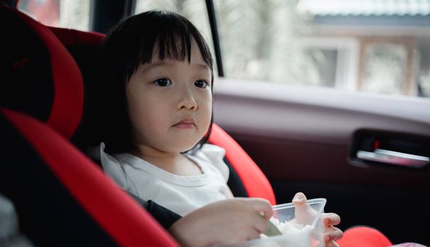 Asiatique mignonne fille déjeunant dans le siège auto. Concept pour la vie de famille en voiture. Repas sur le pouce. - Photo, image