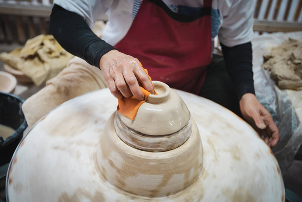 ろくろに白い粘土の陶器を作る陶芸家。手は土鍋からボウルを彫刻します。芸術創造文化伝統手芸. - 写真・画像